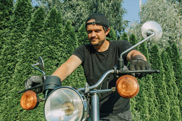 Lächelnder Mann begutachtet Retro-Motorrad im Garten - VSNF01207