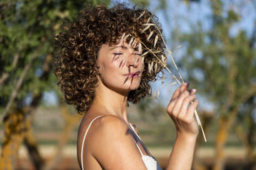 Woman with eyes closed holding twig at sunny day - LMCF00419