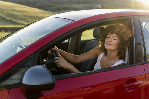 Lächelnde Frau mit geschlossenen Augen fährt rotes Auto - LMCF00432