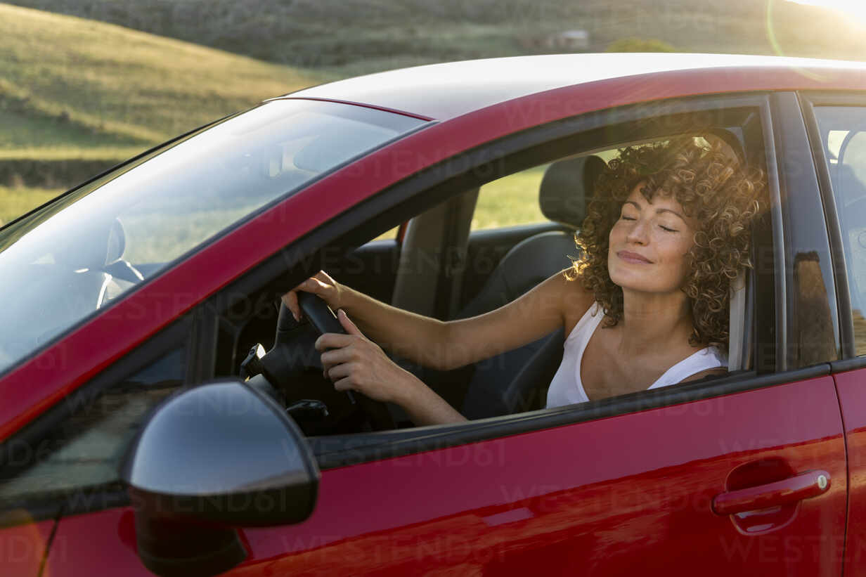 Lächelnde Frau mit geschlossenen Augen fährt rotes Auto