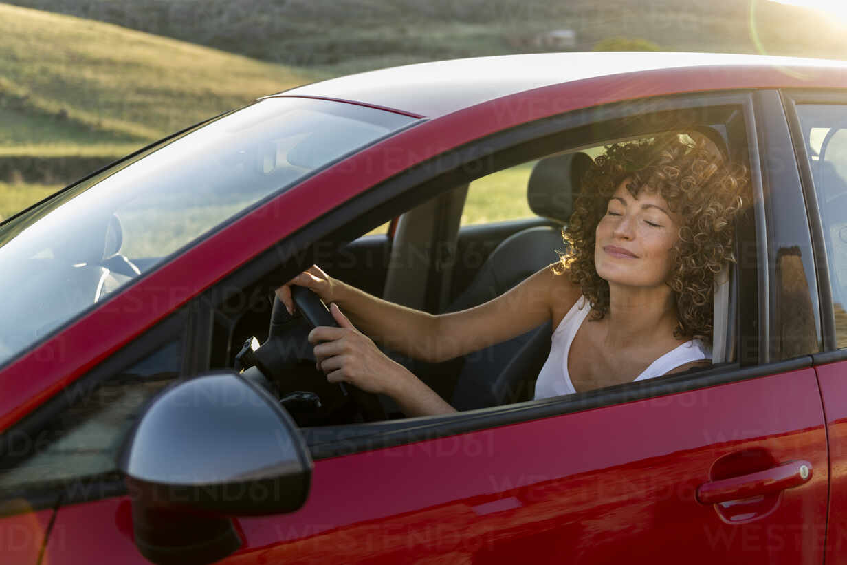 Smiling woman with eyes closed driving red car stock photo