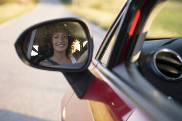 Reflection of happy woman in side view mirror of car - LMCF00435