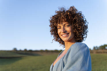 Glückliche Frau mit lockigem Haar bei Sonnenuntergang - LMCF00448