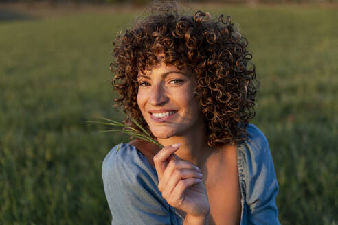 Glückliche Frau mit lockigem Haar hält Gras - LMCF00453