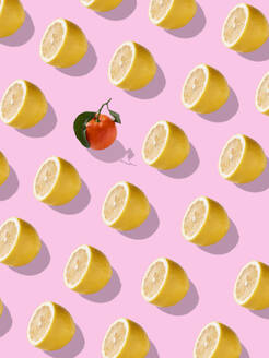 Full frame background of ripe juicy lemon halves and lonely orange with green leaves placed on bright pink backdrop - ADSF45462