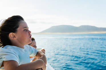 Side view of little girl and boy standing on seashore in sunlight while enjoying summer vacation together during weekend at sunset time - ADSF45508