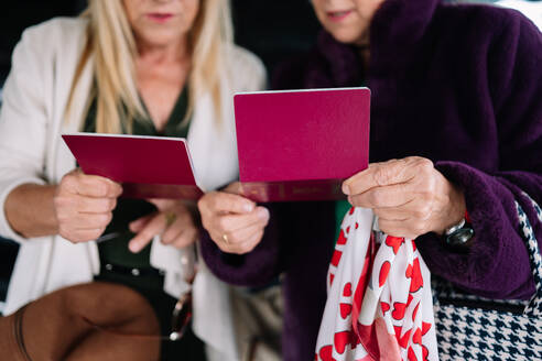 Crop focused elderly female tourists in casual outfits checking information in passports together before flight in airport during trip - ADSF45513