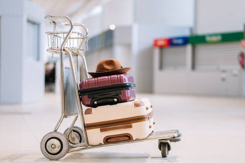 Colorful suitcases and hat placed on trolley in modern airport terminal before flight during trip - ADSF45517