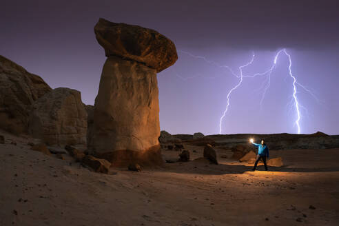 Unrecognizable tourist with a lantern standing on sandy ground with light while admiring a rocky landscape with stone ledges in the late afternoon - ADSF45521