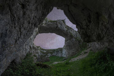 Front view of Mulagljufur Canyon with arched rocky formations surrounded by green trees growing under starry night sky located in Iceland - ADSF45548