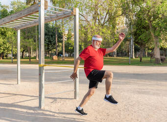 Full body of a strong elderly athlete in sportswear exercising with an elastic resistance band during an intense fitness workout on a sports field - ADSF45578