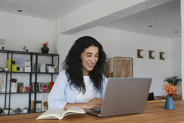 Smiling woman studying with laptop at cafe - SYEF00507