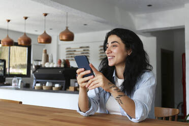 Lächelnde Frau mit Smartphone in einem Café - SYEF00509