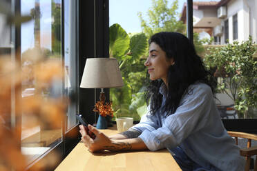 Smiling woman looking out of window sitting in cafe - SYEF00511