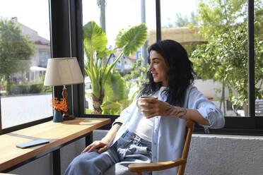 Smiling woman enjoying coffee sitting in cafe - SYEF00513