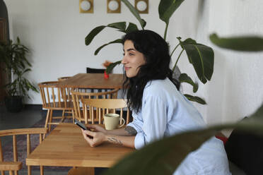 Contemplative woman sitting with smart phone at cafe - SYEF00515