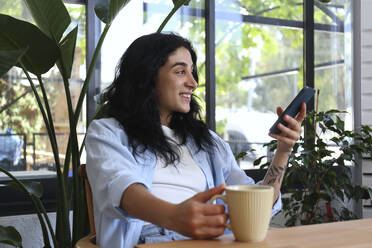Smiling woman holding smart phone at cafe - SYEF00516