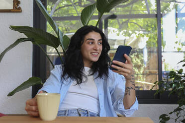 Happy woman holding mobile phone at cafe - SYEF00517