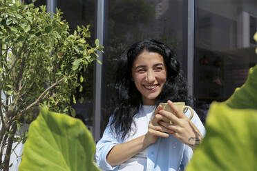 Smiling woman holding coffee cup outside cafe - SYEF00520