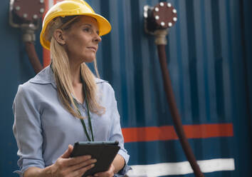 Contemplative engineer wearing hardhat holding tablet PC - AMWF01584