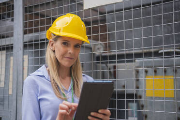 Engineer holding tablet PC near metal fence - AMWF01587