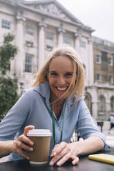 Lächelnde Geschäftsfrau mit Einwegbecher in einem Straßencafé - AMWF01598