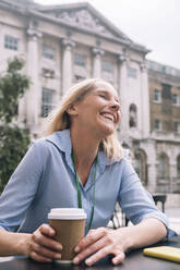 Fröhliche Geschäftsfrau lachend mit Einwegbecher im Café - AMWF01599