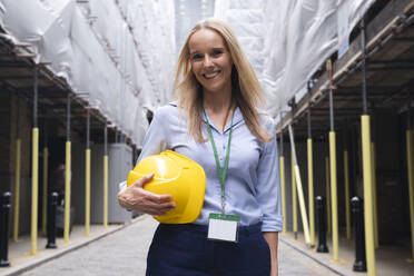 Lächelnder Ingenieur mit Schutzhelm auf einer Baustelle - AMWF01614