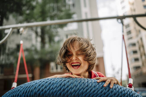 Smiling boy playing on swing at park - ANAF01785