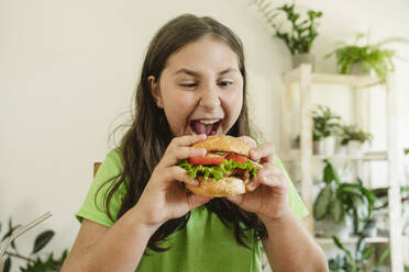 Girl holding burger with open mouth at home - OSF01877