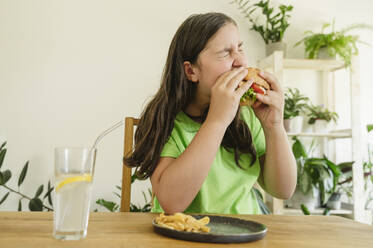 Girl eating hamburger with french fries and soda at home - OSF01880