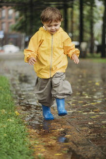 Junge in gelbem Regenmantel spielt im Park - ANAF01789
