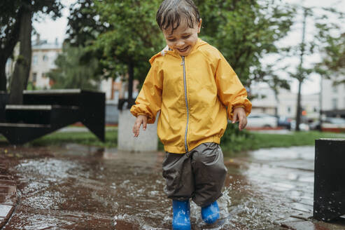 Happy boy splashing water in puddle at park - ANAF01794