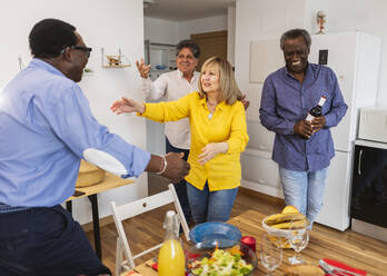 Glückliche ältere multikulturelle Freunde, die zum Abendessen nach Hause kommen - JCCMF10595