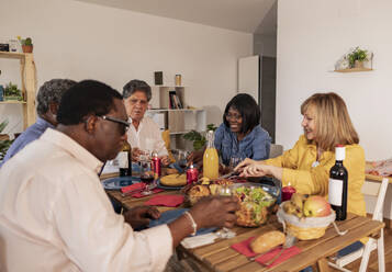 Multi-cultural senior friends having dinner sitting at dining table - JCCMF10612