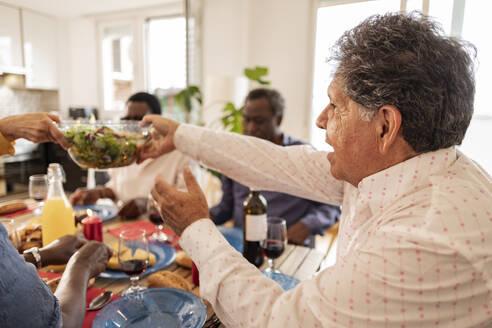Älterer Mann reicht Salatschüssel an Freund zu Hause - JCCMF10616