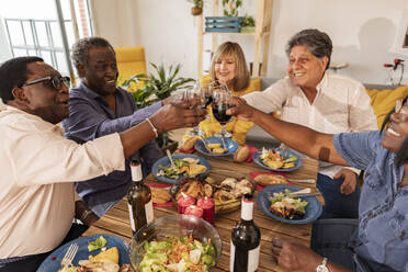 Multi-cultural senior friends toasting wineglasses sitting at dining table - JCCMF10621