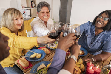 Happy senior multiracial friends toasting wineglasses at dinner party - JCCMF10624
