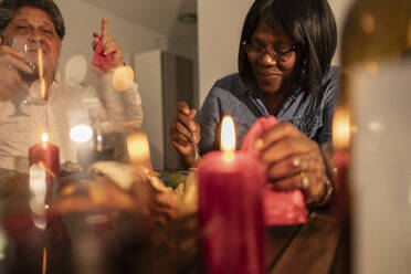 Lächelnde ältere Frau beim Essen mit Kerzen auf dem Tisch zu Hause - JCCMF10626