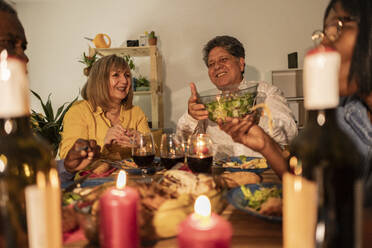 Happy senior friends enjoying dinner with candles on table at home - JCCMF10627