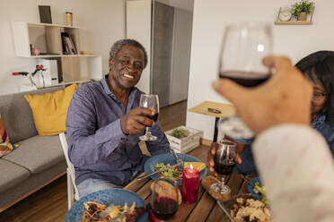 Smiling senior man enjoying wine with friends at dinner party - JCCMF10629