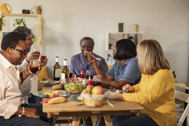 Happy senior multi-cultural friends having food at dinner party - JCCMF10633