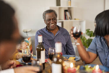 Glücklicher älterer Mann im Gespräch mit einem Freund, der zu Hause ein Weinglas hält - JCCMF10636