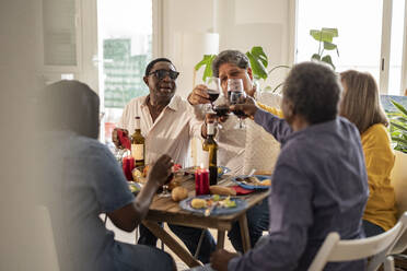 Ältere Freunde stoßen am Esstisch sitzend mit Getränken an - JCCMF10638