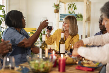 Happy senior women toasting wine sitting with friends at home - JCCMF10641