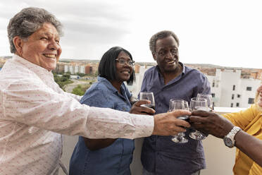 Happy senior friends enjoying wine with each other in balcony - JCCMF10651