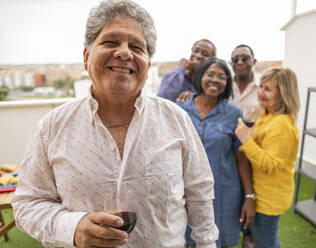 Glücklicher älterer Mann hält Weinglas mit Freunden im Hintergrund - JCCMF10663