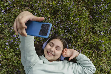 Fröhliches Mädchen fängt einen Moment mit ihrem Smartphone ein, während sie auf dem üppigen grünen Gras faulenzt - OSF01888