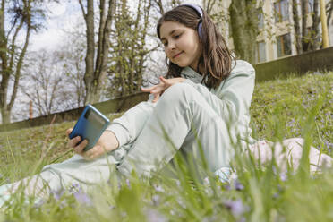 Eine glückliche junge Frau fängt einen Moment in der Natur mit ihrem Smartphone ein und posiert für ein Selfie im Garten - OSF01889