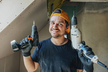 Smiling man holding drills in attic - VSNF01212